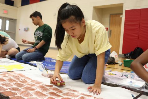 Junior Tammy Ding uses a sponge to paint bricks in the middle of 2021's banner. 2021's banner was a representation of various items on a filmstrip. "Filmstrips are vintage, and we [wanted to] have different elements of the 90s in each picture," Ding said.
