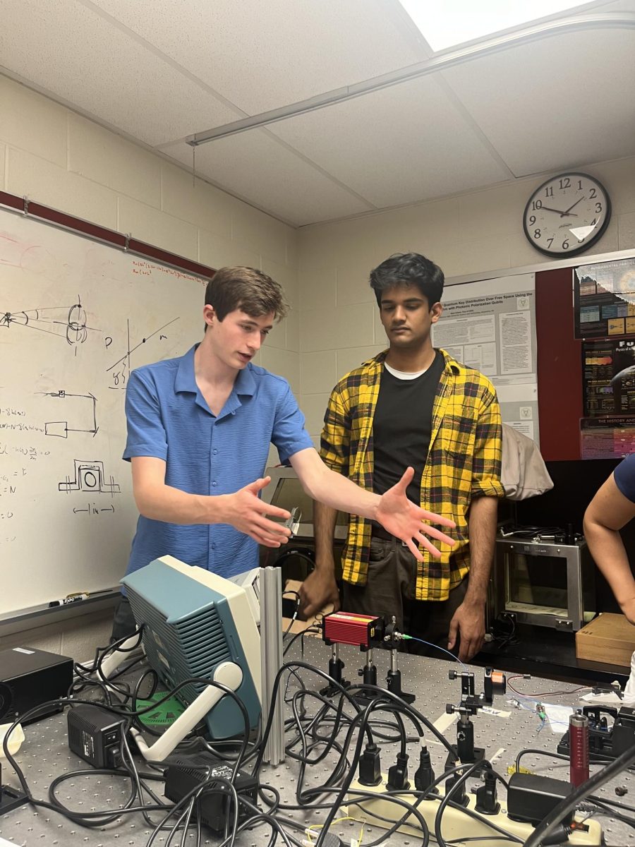 Gesturing+towards+their+project%2C+senior+Alec+Riso+describes+the+mechanisms+of+the+group%E2%80%99s+QKD+system+alongside+senior+Karthik+Thyagarajan.+%E2%80%9CThis+laser+generates+a+stream+of+photons.+We+lined+it+up+with+a+collimated+lens%2C+%5Bwhich%5D+focuses+the+laser+into+an+optical+fiber%2C%E2%80%9D+senior+Connor+Whiting+said.+%E2%80%9CThe+optical+fibers+%5Bpreserve+or+maintain%5D+are+how+you+measure+the+polarization+state+of+the+photon%2C+which+lets+us+do+the+encryption+protocol.%E2%80%9D+